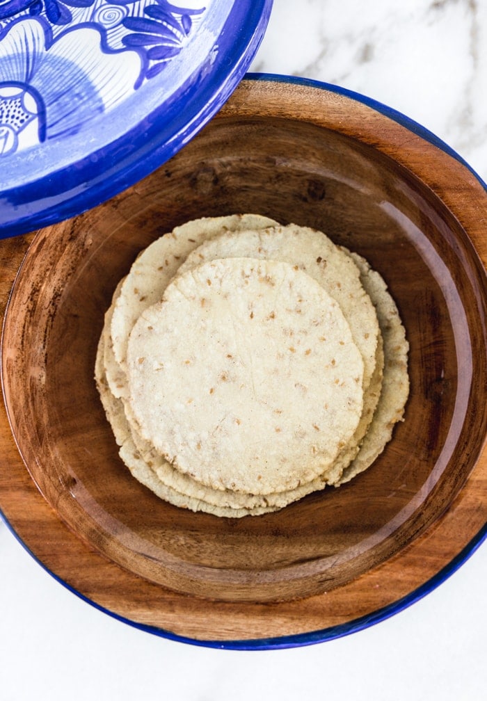 homemade corn tortillas stacked in a blue and white tortilla holder