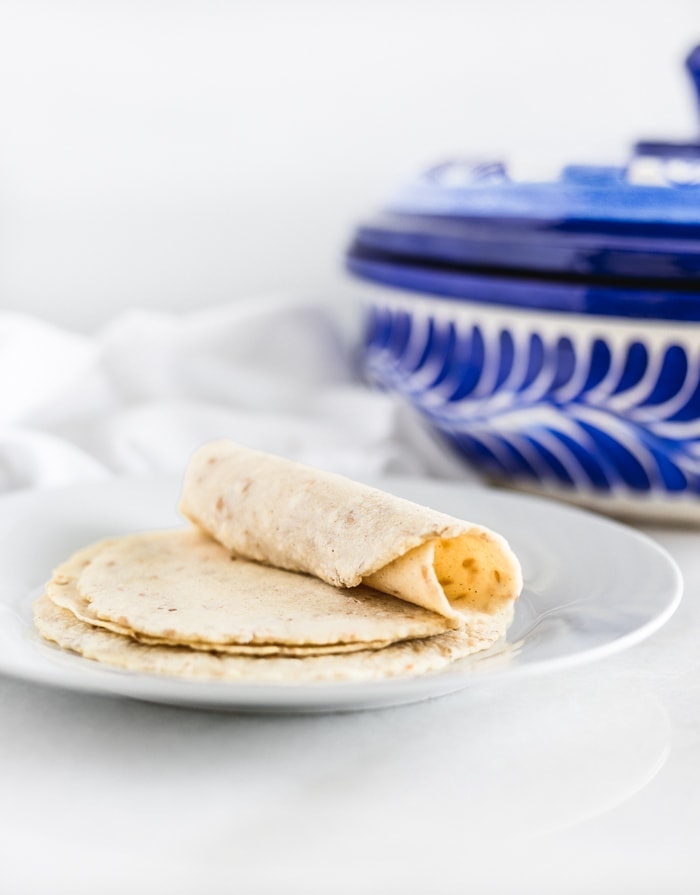 homemade corn tortillas on a plate with one tortilla rolled up