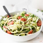 closeup of zucchini noodle salad with tomatoes, avocado and feta in a white bowl.