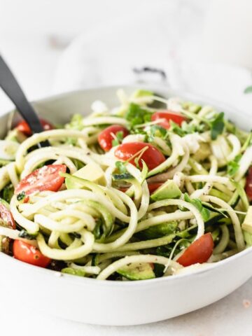 closeup of zucchini noodle salad with tomatoes, avocado and feta in a white bowl.