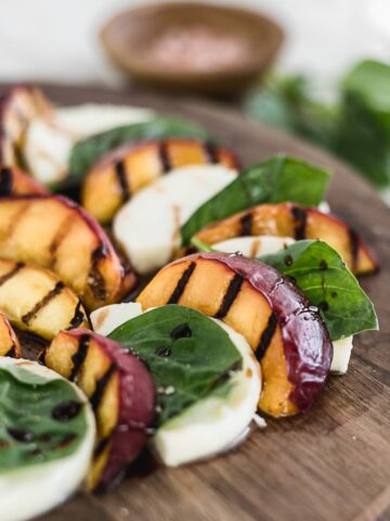 closeup of grilled peach caprese salad on a wooden cutting board.