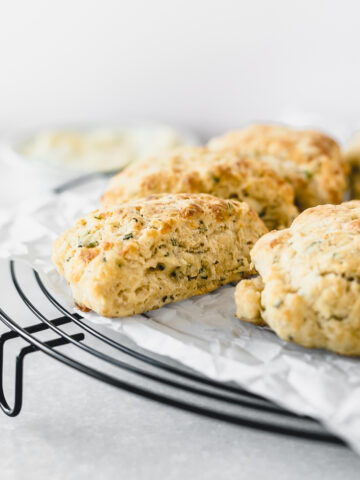 closeup of rosemary parmesan scones on top of a parchment lined black cooling rack.