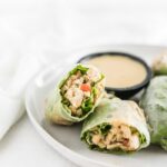 Thai peanut chicken salad spring rolls cut in half on a white plate with peanut dipping sauce.