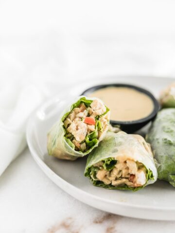 Thai peanut chicken salad spring rolls cut in half on a white plate with peanut dipping sauce.