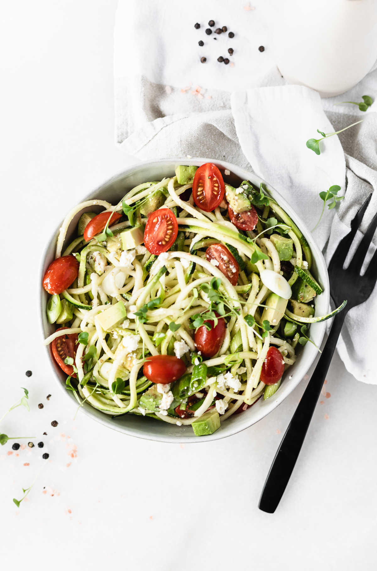 overhead view of avocado tomato zucchini salad in a bowl with a black serving fork beside it.