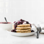 stack of quinoa pancakes on a plate topped with berry compote and yogurt.