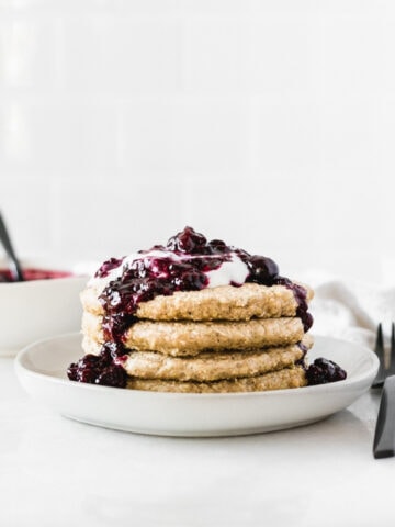 stack of quinoa pancakes on a plate topped with berry compote and yogurt.