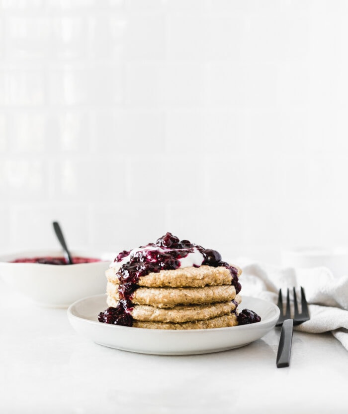 stack of quinoa pancakes on a plate topped with berry compote and yogurt..