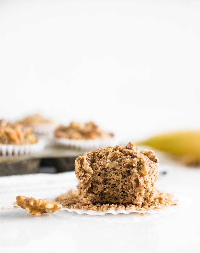 A bite taken out of a healthy blender gluten-free banana nut muffins and more muffins behind it.