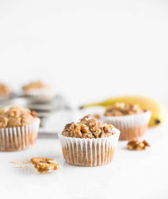 Healthy blender Gluten-free banana nut muffins on a white counter with walnuts and a banana around them.