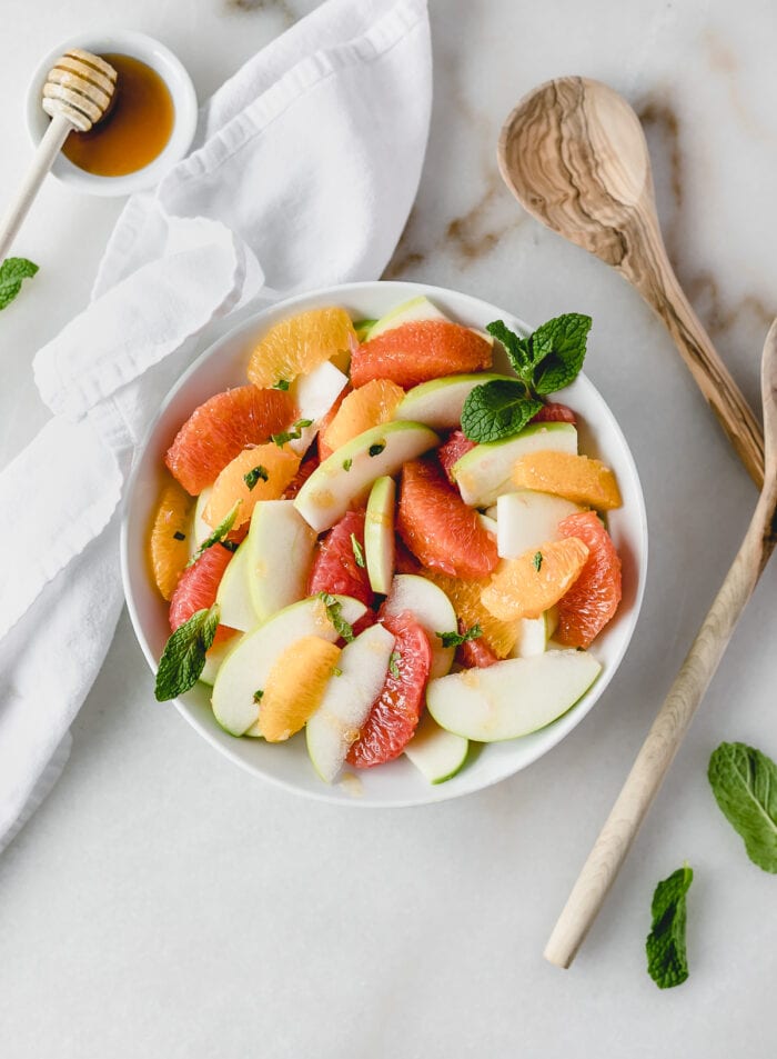 overhead view of a grapefruit apple citrus salad in a white bowl topped with mint.