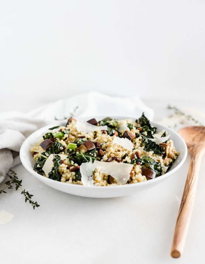 white bowl with eggplant and kale quinoa salad with a wooden spoon beside it.