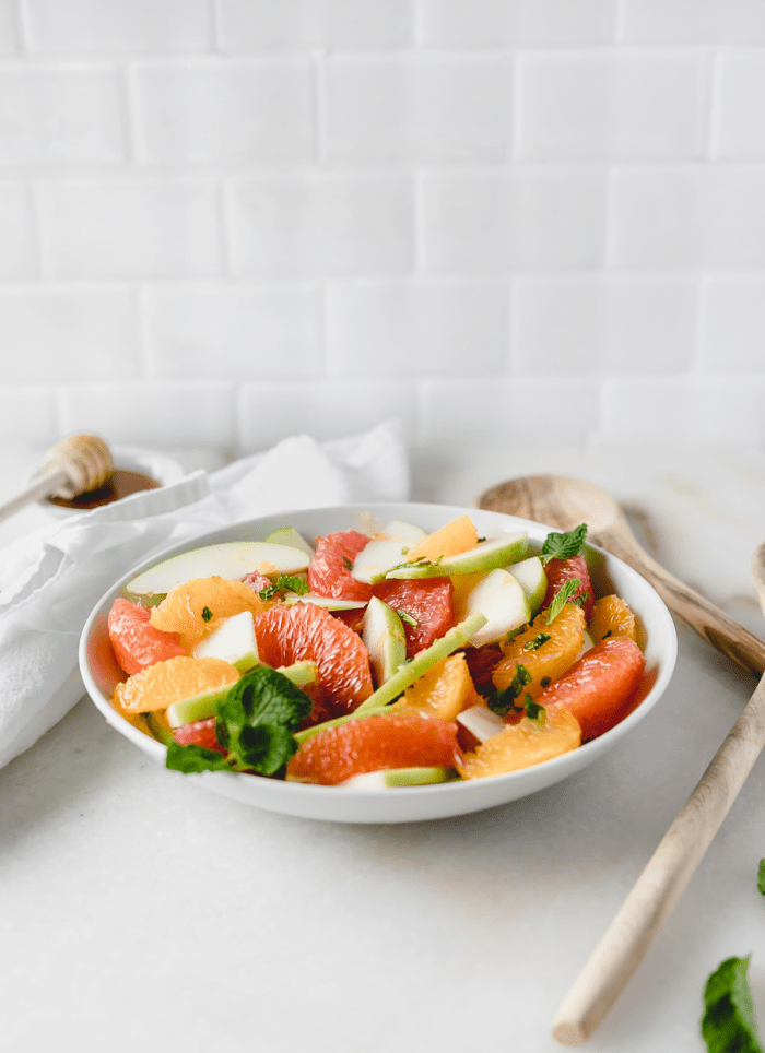 granny smith apple citrus salad topped with fresh mint in a white bowl.