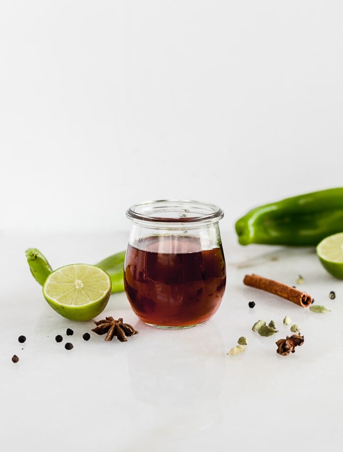 hatch chile simple syrup in a glass jar with chiles and spices around the jar.