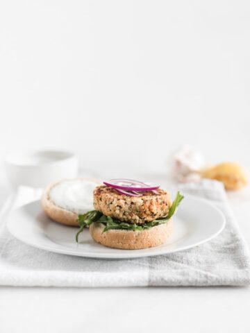 Easy quinoa salmon burgers with red onion and arugula on a white plate.