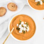 top view of healthy roasted butternut squash soup topped with pumpkin seeds and goat cheese with a gold spoon inside.