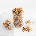 Healthy banana bread granola in a mason jar on top of a napkin with granola and banana slices on the side.