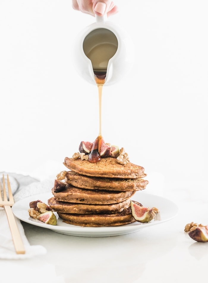 Healthy oatmeal pumpkin pancakes with walnuts and figs getting syrup poured over them.