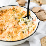 hot broccoli dip in a white skillet with a spoon in it.