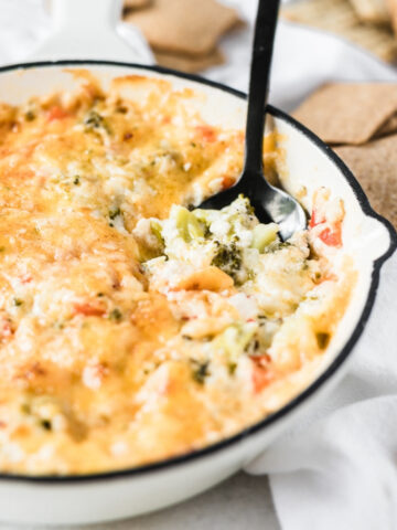 hot broccoli dip in a white skillet with a spoon in it.