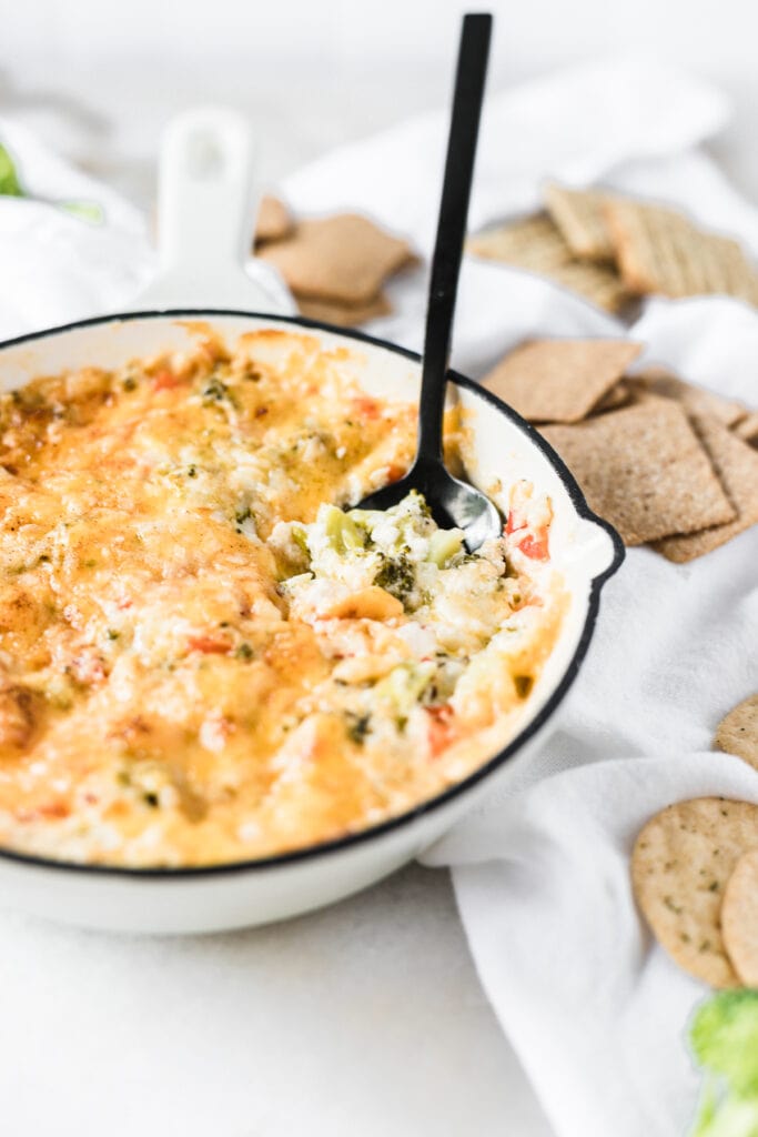 hot broccoli dip in a white skillet with a black spoon in it.