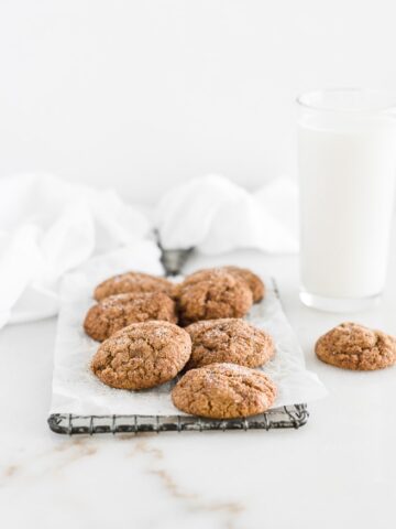 pumpkin snickerdoodles on a wire cooling rack with a white towel and glass of milk behind them.