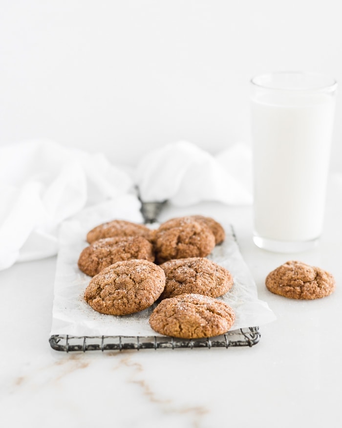 pumpkin snickerdoodles on a wire cooling rack with a white towel and glass of milk behind them.