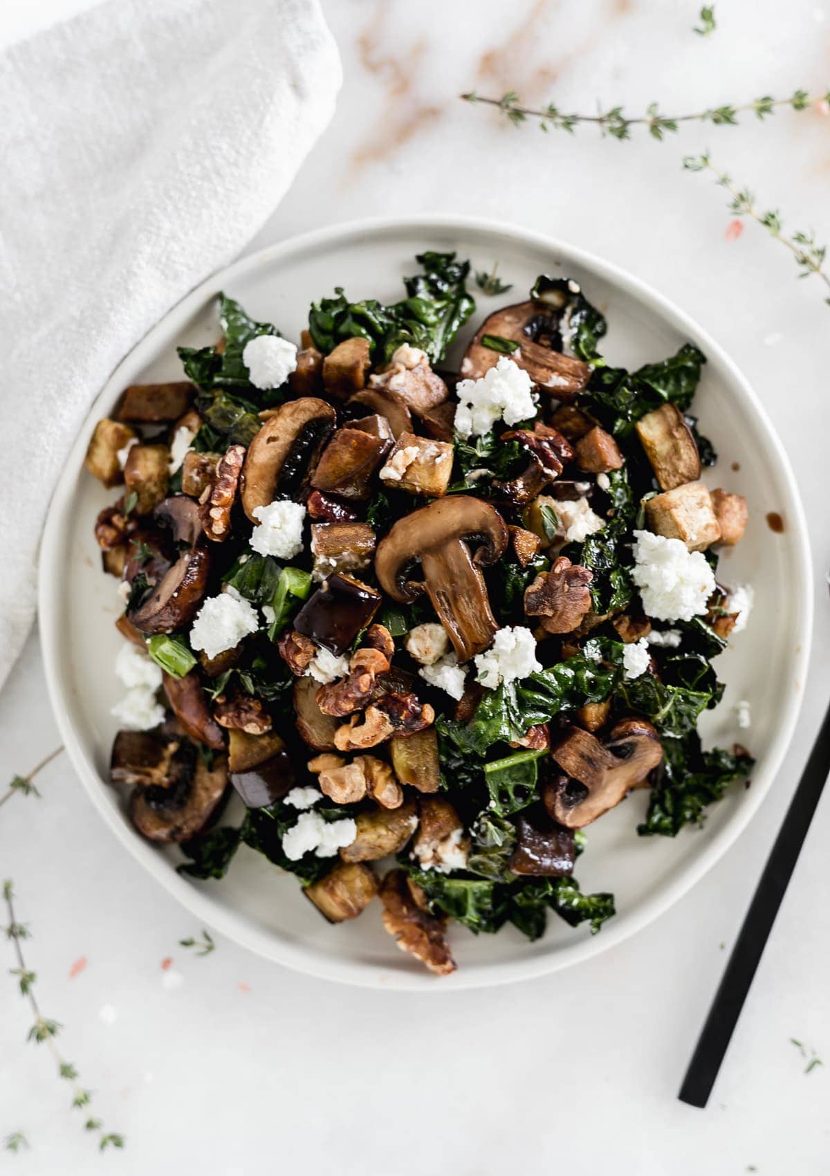 Warm eggplant, mushroom, and kale salad on a white plate.