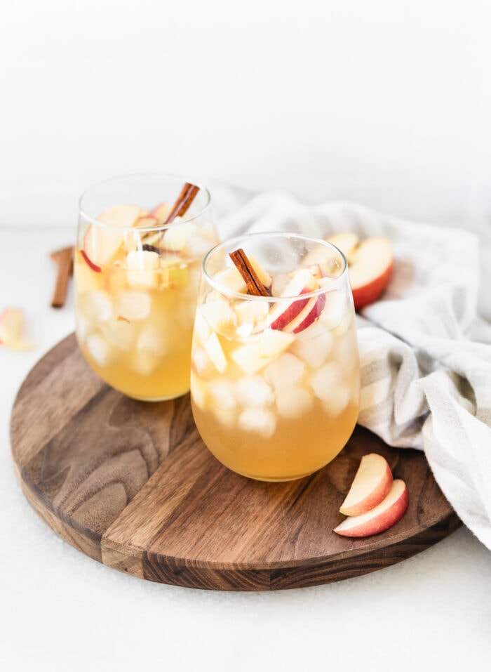 two glasses of apple cider sangria on a wooden board with a grey striped linen and a cut apple.