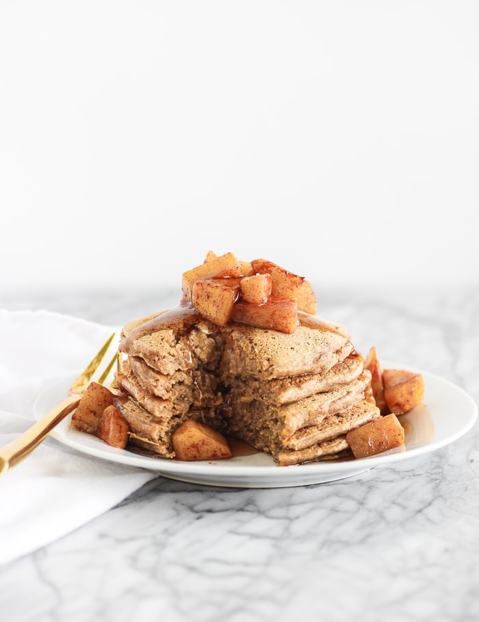 healthy apple cinnamon pancakes stacked on a white plate with a bite taken out.