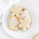 overhead view of snowflake and christmas tree sugar cookies with white icing on a white plate.