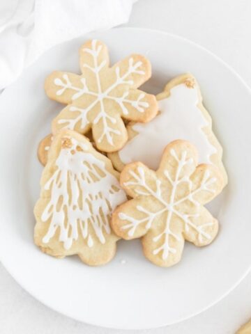 overhead view of snowflake and christmas tree sugar cookies with white icing on a white plate.