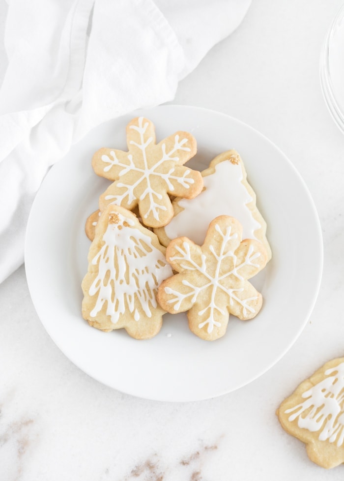 Overhead view of snowflake and christmas tree cutout sugar cookies with white icing on a white plate.