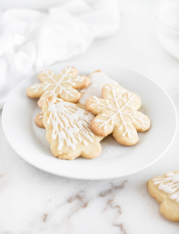 snowflake and christmas tree cutout sugar cookies with icing on a white plate.