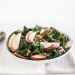 fall kale salad with sorghum, apples and pears in a white bowl.