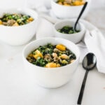 Sausage, Kale and Butternut Squash Soup in a white bowl with a black spoon beside it.