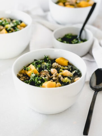 Sausage, Kale and Butternut Squash Soup in a white bowl with a black spoon beside it.