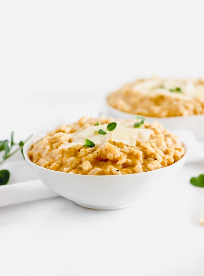 pumpkin risotto in a white bowl topped with parmesan cheese and herbs.