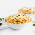 creamy pumpkin risotto in a white bowl with parmesan and herbs on top.