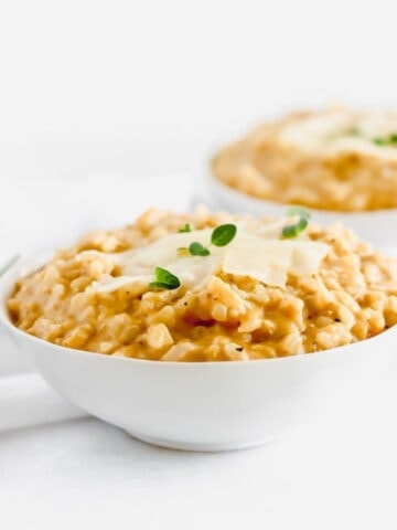 creamy pumpkin risotto in a white bowl with parmesan and herbs on top.