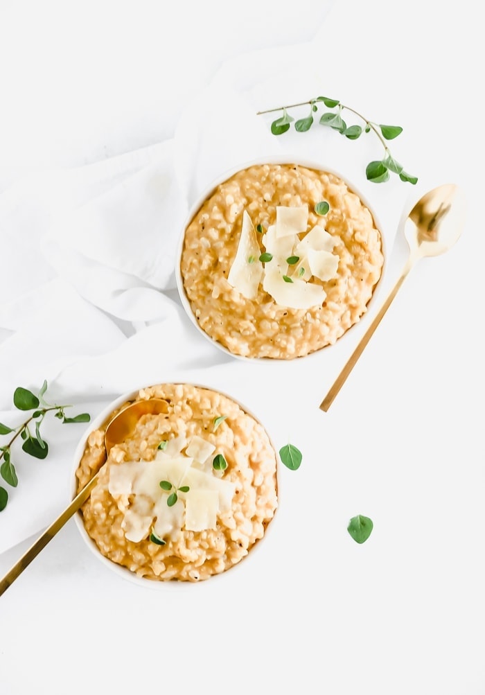 overhead view of creamy pumpkin risotto in 2 white bowls topped with parmesan and herbs.