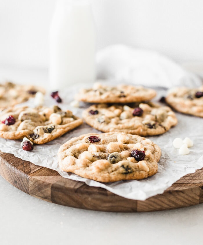 closeup of a cranberry white chocolate bliss cookie on a wooden board lined with parchment with more cookies behind it.