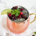 Closeup of a cranberry Moscow mule in copper cup topped with fresh cranberries, mint, and lime.