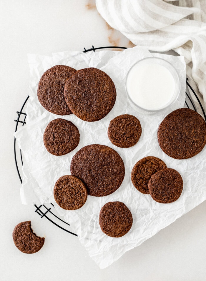 overhead view of two sizes of gingersnap cookies on a parchment lined rack with a glass of milk.