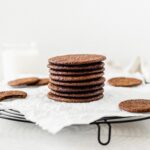 gingersnaps stacked on top of each other on a cooling rack lined with parchment.