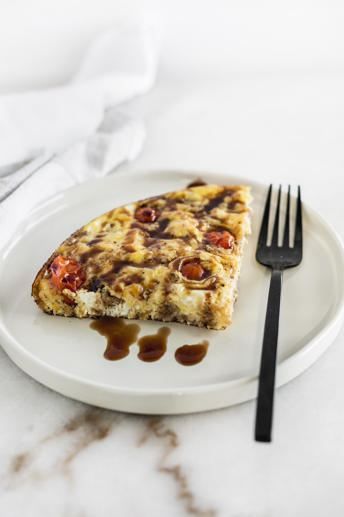 A slice of Italian sausage and tomato frittata on a white plate.