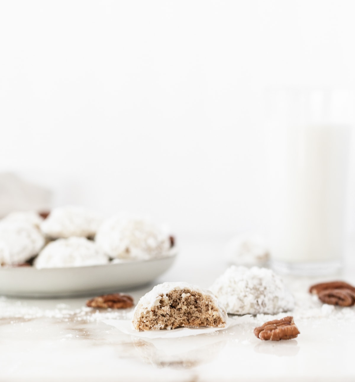 Close up of half of a pecan snowball cookie and more cookies behind it on a plate.