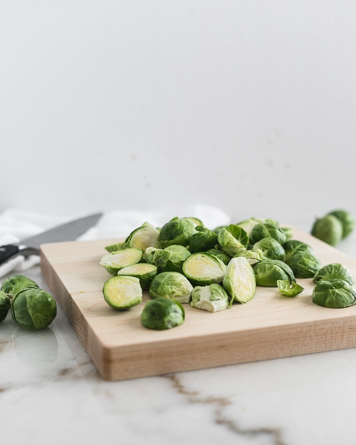 fresh brussels sprouts cut in half on a wooden cutting board.