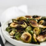 closeup of simple balsamic roasted brussels sprouts on a white plate.