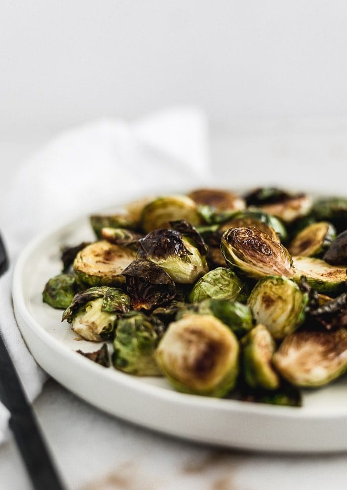 closeup of simple balsamic roasted brussels sprouts on a white plate.